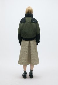 Casaco puffer curto em verde escuro e preto, combinado com uma saia bege acolchoada de comprimento médio. Apresenta um colarinho alto e um design robusto.