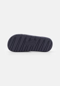 Dunkelblauer Sneakersohle mit strukturiertem Oberflächen, die horizontale und vertikale Rillen aufweist, sowie einem geprägten Logo-Detail in der Mitte.