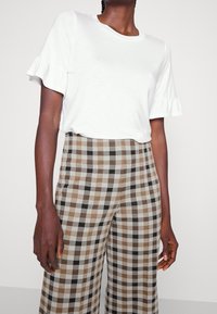 Witte korte mouwen top met gerimpelde manchetten, gecombineerd met een beklede broek met brede benen in beige, bruin en zwart. Zachte stof en een relaxte pasvorm.