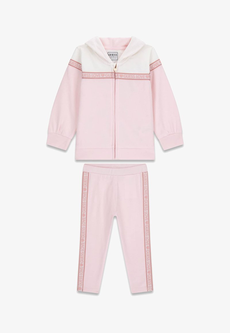 Set composto da felpa con cappuccio e leggings rosa chiaro in tessuto morbido. La felpa presenta una sezione superiore bianca e una cerniera, mentre i leggings hanno strisce con il logo.