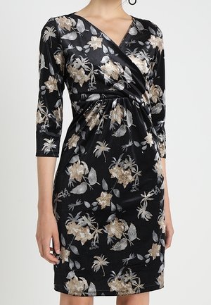 Zwarte omslagjurk tot op de knie met beige en zilveren bloemmotieven en driekwart mouwen, gedragen door een persoon.