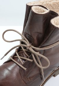 Braune Leder-Stiefelette mit einem weichen, hellbraunen Innenfutter, runder Zehenform und einfachem Schnürdesign. Texturierte Oberfläche mit minimaler Naht.