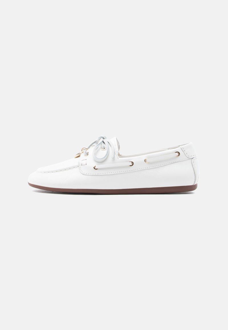 Mocassin loafer en cuir blanc avec détail nœud, œillets dorés et semelle en caoutchouc marron, présenté de profil sur un fond uni.