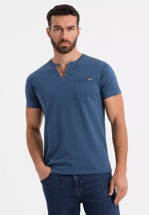 Camiseta de algodón azul con cuello redondo, tapeta de tres botones con detalles de madera y bolsillo en el lado izquierdo del pecho.