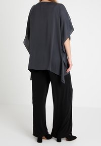 Ciemnoszara, lekka bluzka o luźnym kroju i szerokich rękawach, zestawiona z czarnymi, szerokimi spodniami i czarnym obuwiem.