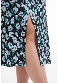 Robe noire à motif floral avec des fleurs bleues et blanches. Présente une texture côtelée et une fente latérale dévoilant la peau en dessous.