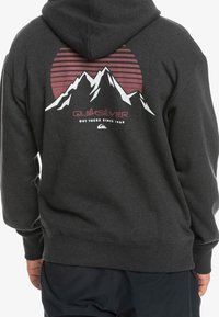 Felpa nera con cappuccio, caratterizzata da una grafica di montagne e un tramonto, con righe e il logo "Quiksilver" in rosso e bianco.