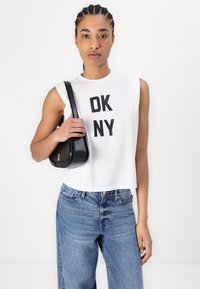 Fehér, ujjatlant crop top fekete "OK NY" felirattal, magas derekú kék farmernadrággal és fekete keresztpántos táskával párosítva.