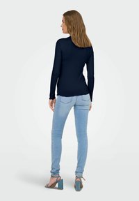 Maglia a maniche lunghe a coste di colore blu navy abbinata a jeans skinny azzurri e sandali blu con tacco a blocco, con un dettaglio di spacco sul fondo.