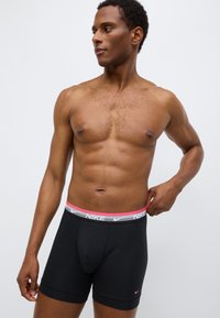 Μαύρα ανδρικά εσώρουχα τύπου boxer της Nike με γκρι και ροζ ελαστική μέση που φέρει το λογότυπο της μάρκας, με λείο ύφασμα και εφαρμοστή σχεδίαση.