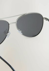 Hopea metallinen aviator-tyylinen aurinkolasit tummilla linsseillä, varustettuna kaksoissillalla, läpinäkyvillä nenäpadilla ja ohuilla mustilla varsilla.