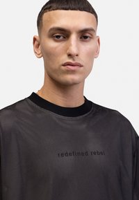 Sort mesh t-shirt med rund halsudskæring og korte ærmer, med den trykte tekst "redefined rebel" på forsiden.