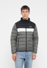 Puffervest i sort, grå og hvid. Har en høj krave, lynlåslukning foran og vandret paneldesign. Glat tekstur med quiltede sektioner.