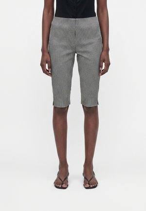 Zwart-wit geruite knielange shorts gedragen met een zwart topje en zwarte sandaaltjes met bandjes bij een staande persoon tegen een witte achtergrond.