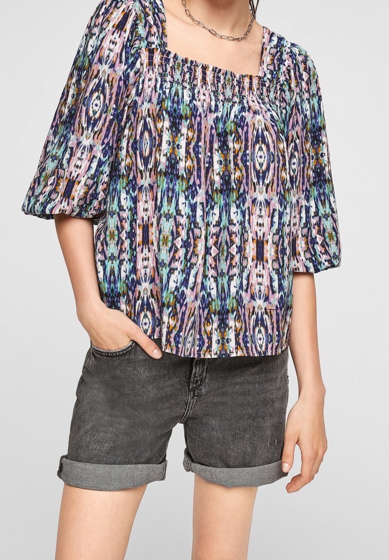 Flerfärgad mönstrad blus med fyrkantig halsringning, samlad textur och puffärmar, i kombination med rullade svarta denimshorts.