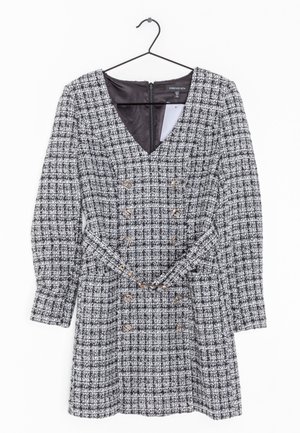 Mustavalkoruudullinen pitkähihaiset mekko, jossa on V-kaula-aukko, kaksiriviset kultaiset napit ja siihen sopiva vyö. Mekko roikkuu mustassa henkariassa.