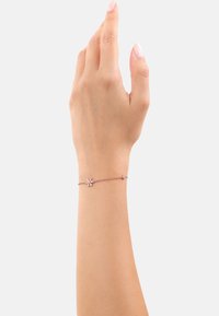 Bracciale in oro rosa con una delicata catena, caratterizzato da un piccolo design floreale e una pietra accentuata singola, indossato su una mano con un tono di pelle chiaro.