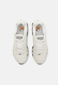 Paire de baskets blanches Nike Air Max avec des accents noirs, lacets attachés, et logo Air Max visible sur la languette et les semelles intérieures.