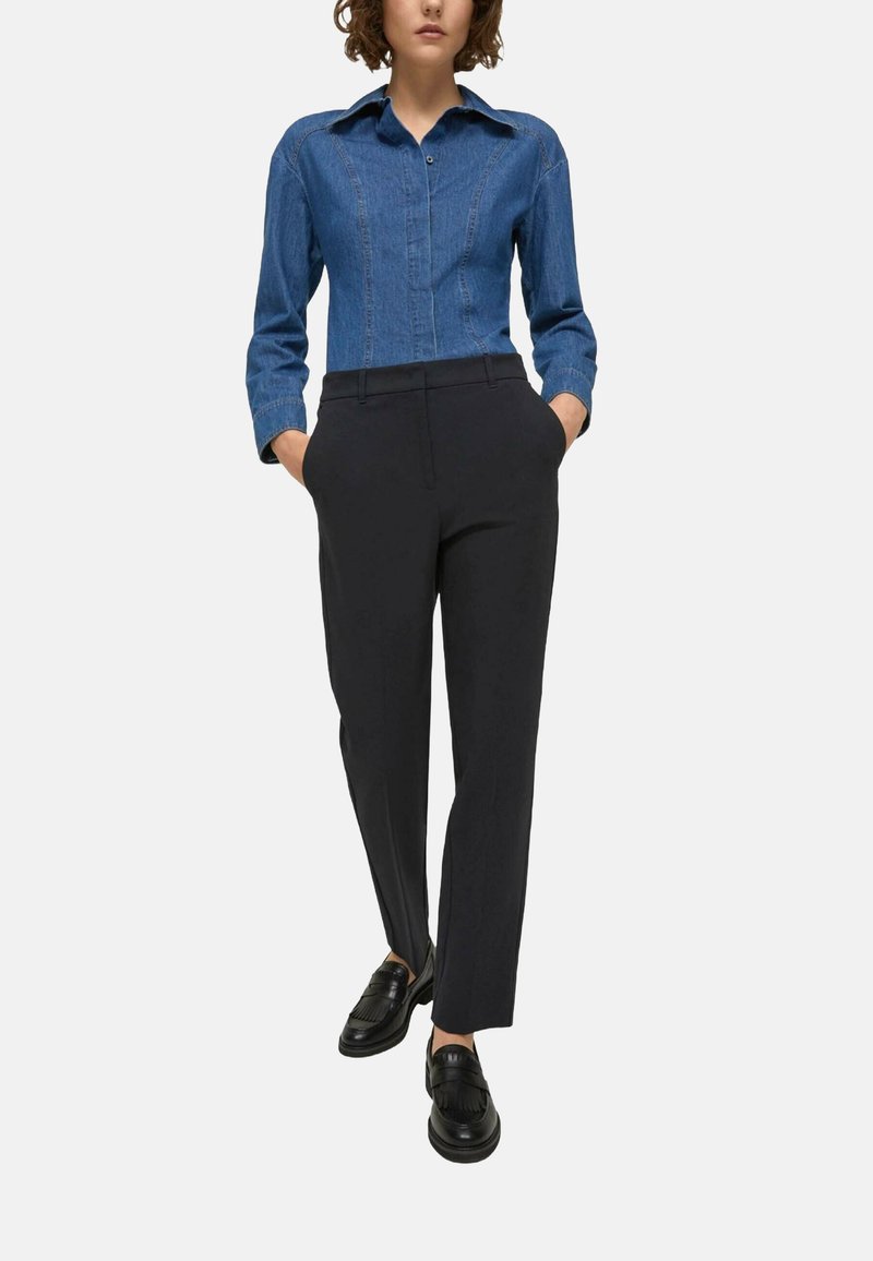 Camicia di jeans blu con colletto button-down e maniche lunghe, abbinata a pantaloni sartoriali neri e mocassini neri.