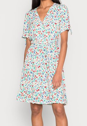 Femme portant une robe portefeuille à manches courtes, longueur genou, avec un imprimé floral rouge, bleu et vert, et une ceinture à la taille.