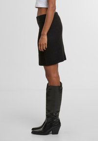 Černá pletená sukně se přiléhavým pasem, doplněná o vysoké černé kožené boty na podpatku s blokovým podpatkem a špičatou špičkou.