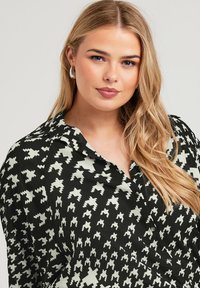 Blusa de manga larga con estampado geométrico en negro y crema, diseño con cuello y textura de tela suave, con detalles de botones.