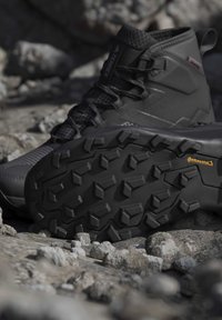 Black hiking boot with rugged Continental rubber sole placed on rocky terrain outdoors.