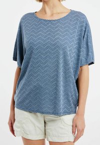 Top azul de manga corta hecho de tela texturizada con un patrón de zigzag, con un escote amplio y un corte relajado. Combinado con pantalones cortos beige claro.