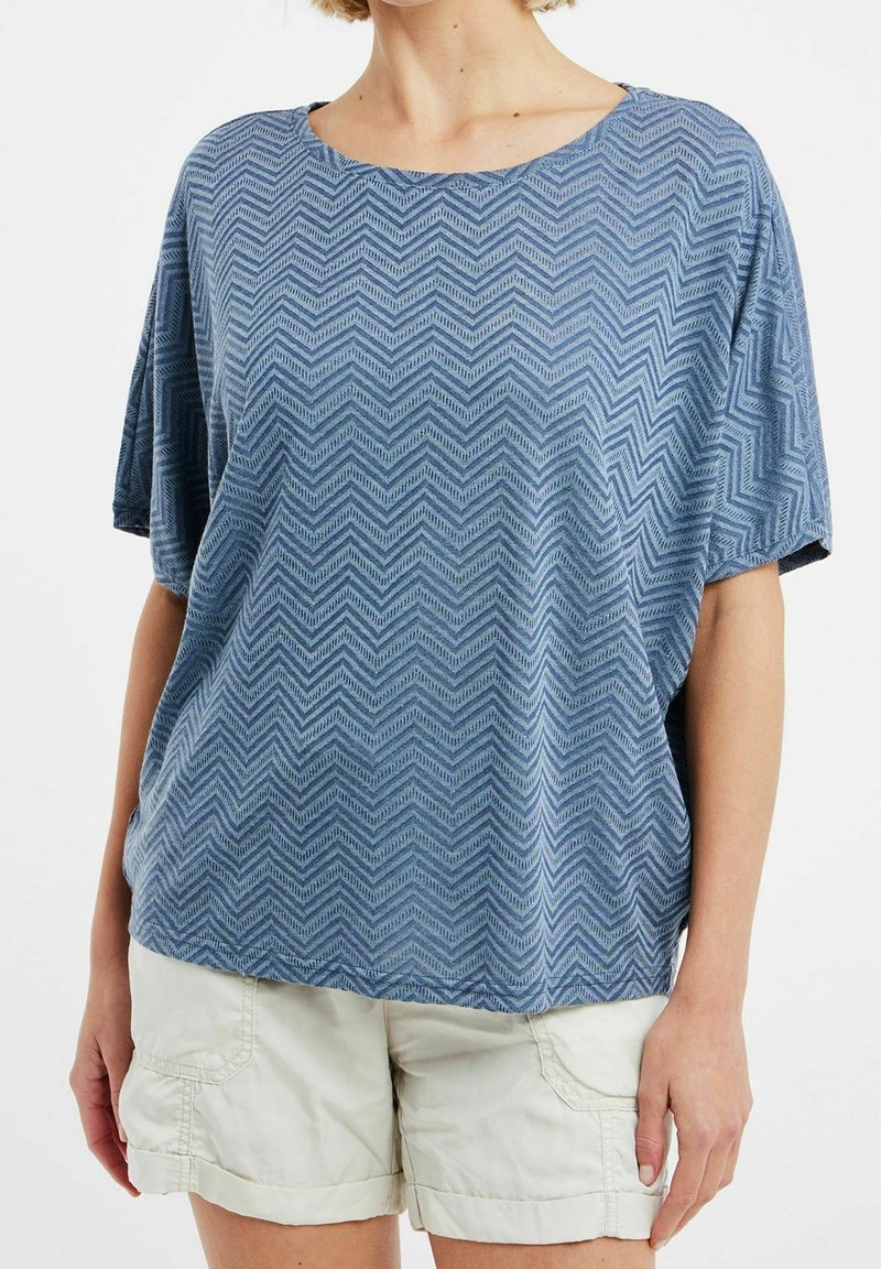 Top azul de manga corta hecho de tela texturizada con un patrón de zigzag, con un escote amplio y un corte relajado. Combinado con pantalones cortos beige claro.