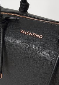 Black textured leather handbag featuring a rose gold "VALENTINO" logo on the front, complemented by a top zipper and knotted handles.