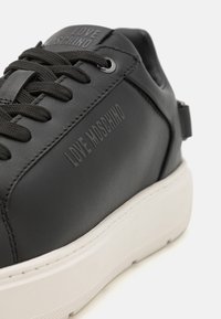 Zwarte leren sneaker met dikke witte zool, voorzien van een reliëf "LOVE MOSCHINO" logo op de tong en een gladde afwerking. Veters voor een veilige pasvorm.