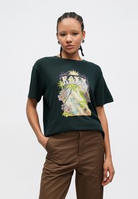 T-shirt en coton vert foncé avec un motif floral coloré, le mot "ROXY" et des éléments de la nature, manches courtes et coupe décontractée.