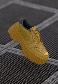 Nike tenisice s gornjim dijelom od žute kože, sivim ovratnikom i debelim, teksturiranim gumenim potplatom koji ima uzorak mreže i perforirane detalje.