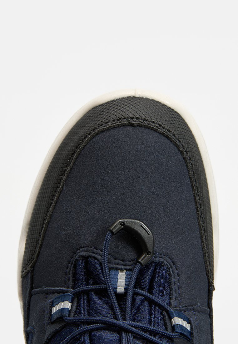 Marineblaue Sportschuh mit einer strukturierten schwarzen Gummispitze, elastischem Schnürsystem und einem glatten Stoffobermaterial. Weiße Sohlenakzente.