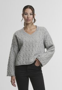 Světlě šedý svetr s kabelovým vzorem, výstřihem do V, širokými rukávy a volným střihem. Jemná textura se složitými pletenými vzory.