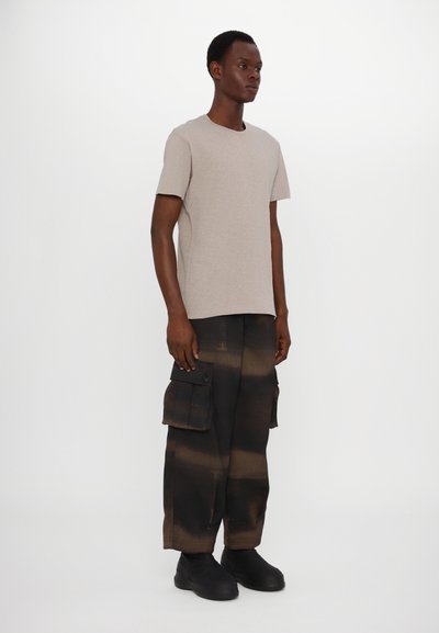Beige t-shirt med kort ärm som matchas med svarta cargobyxor med ett gradientmönster och sidofickor, avslutat med svarta skor.