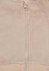 Beige zip-up fleece jacket with a soft texture, featuring a prominent zipper and border. The fabric appears plush and warm.