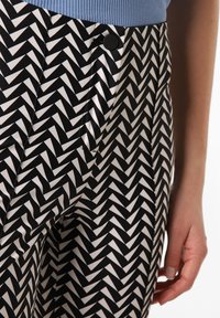 Czarno-białe spodnie w wzór zygzak z gładką teksturą, z detalem w postaci guzika oraz jasnoniebieską prążkowaną talią.