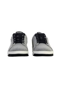 Zapatillas de lona grises con cordones negros, suelas de goma blanca y paneles laterales texturizados. Marca en las lenguas, diseño minimalista sin patrones.