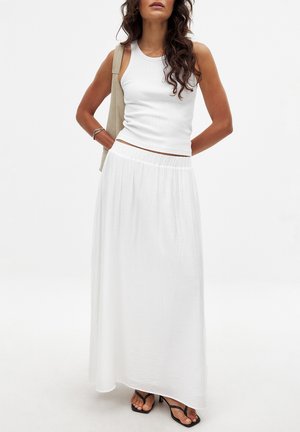Gonna maxi bianca realizzata in tessuto leggero con vita arricciata, abbinata a un top aderente bianco e sandali neri.