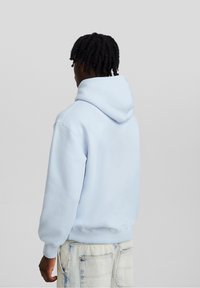 Sudadera con capucha de color azul claro, hecha de una tela suave, con puños y dobladillo de canalé. Presenta un ajuste holgado y un bolsillo tipo canguro.