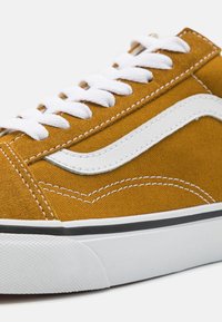 Gule kanvas sneakers med en hvit gummisåle, som har hvite snørebånd og en hvit stripe på siden. Teksturert overflate med kontrasterende sømdetaljer.