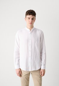 Witte linnen langemouwen overhemd met een Mandarin-kraag, voorzien van subtiele textuur en knoopsluiting, gecombineerd met lichtgekleurde broeken.