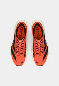 Κόκκινα αθλητικά παπούτσια με μαύρες λεπτομέρειες, επάνω μέρος από δίχτυ, υφασμένα σχέδια και παχύ άσπρο πέλμα. Διαθέτουν κορδόνια και λογότυπο "TERREX" στο εσωτερικό.