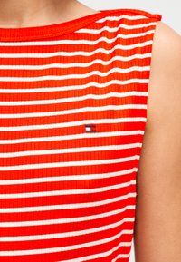 Κόκκινη ριγωτή αμάνικη μπλούζα με οριζόντιες λευκές ρίγες, στρογγυλή λαιμόκοψη και μικρή διακριτική λογότυπη λεπτομέρεια στο στήθος.