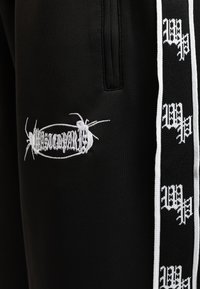 Pantalones de chándal negros con un diseño de hormiga bordado en blanco y un logo en el frente, con una franja contrastante a lo largo del costado.