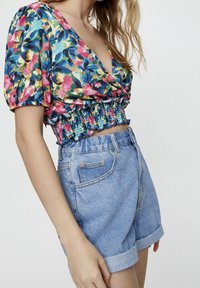Blouse à manches courtes en imprimé floral avec un décolleté en V profond et une taille froncée, associée à un short en denim taille haute bleu clair, retroussé en bas.