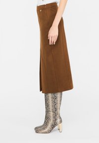 Gonna midi in suede marrone con spacco laterale, abbinata a stivali metallici in stampa snake fino al ginocchio con tacco quadrato.