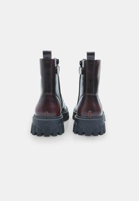 Pruun nahast pahkluusaapad, millel on jäme must kummist tald, külgletid ja tõmbenöörid taga. Suure kontrasti õmblemise detail.