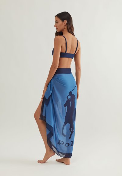 Μπλε κρουαζέ φούστα από ελαφρύ ύφασμα, με σκούρο μπλε σχέδιο σιλουέτας και τη λέξη "Polo". Συνδυάζεται με μπλε τοπ στο ίδιο χρώμα.